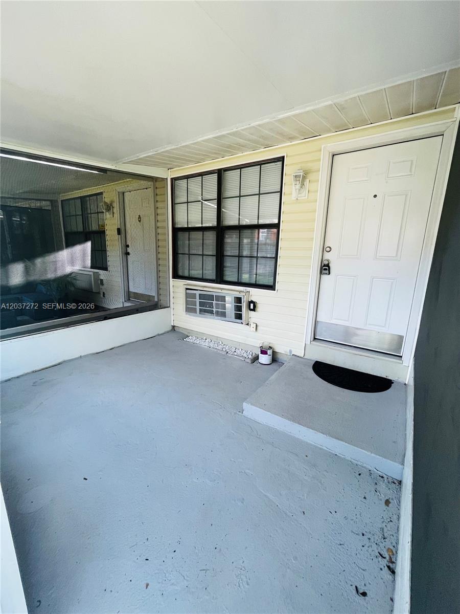 A covered porch features a white door, a window with an air conditioning unit, and flooring — 4251 E Michigan Street # 4251, Orlando FL 32812, ORLANDO, FL