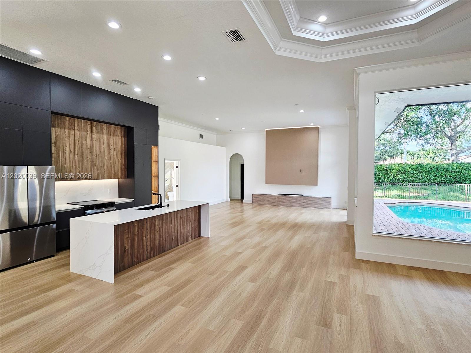 A modern open-concept kitchen and living area features wood cabinetry, white countertops, and pool views — 18951 SW 30th St, Miramar FL 33029, MIRAMAR, FL