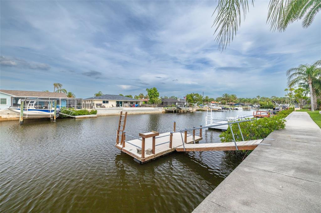 A concrete walkway leads to a floating dock on a canal with residential houses nearby — 9908 SAN SIERRA WAY, PORT RICHEY, FL