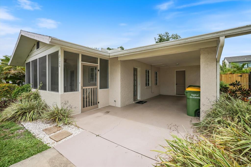 A single-story house exterior featuring a screened-in porch, a concrete carport, and a green trash bin — 2126 HYDE PARK STREET, SARASOTA, FL