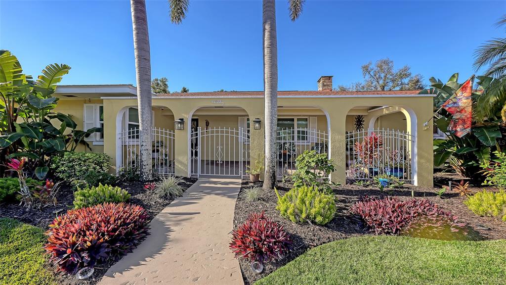 A yellow single-story house features an arched front porch, white metal fencing, and landscaped gardens — 844 MAGELLAN DRIVE, SARASOTA, FL
