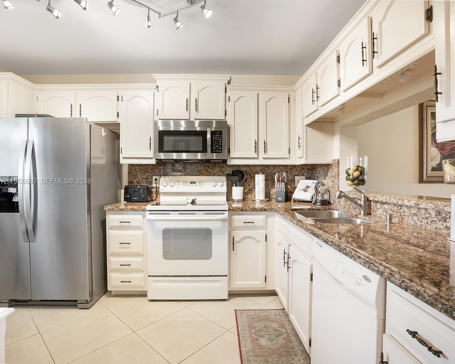 A kitchen features white cabinets, granite countertops, stainless steel appliances, and tile flooring — 3591 Environ Blvd # A404, Lauderhill FL 33319, LAUDERHILL, FL