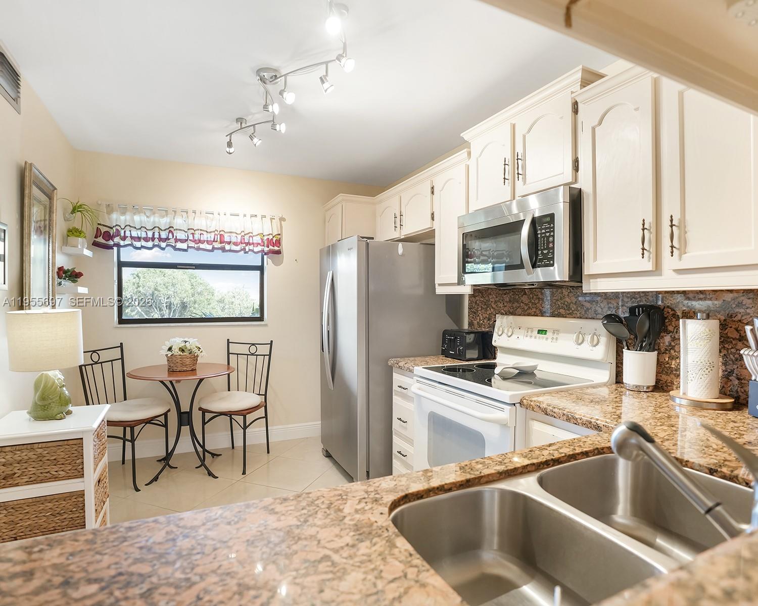 A kitchen features granite countertops, white cabinets, stainless steel appliances, and a small dining area — 3591 Environ Blvd # A404, Lauderhill FL 33319, LAUDERHILL, FL