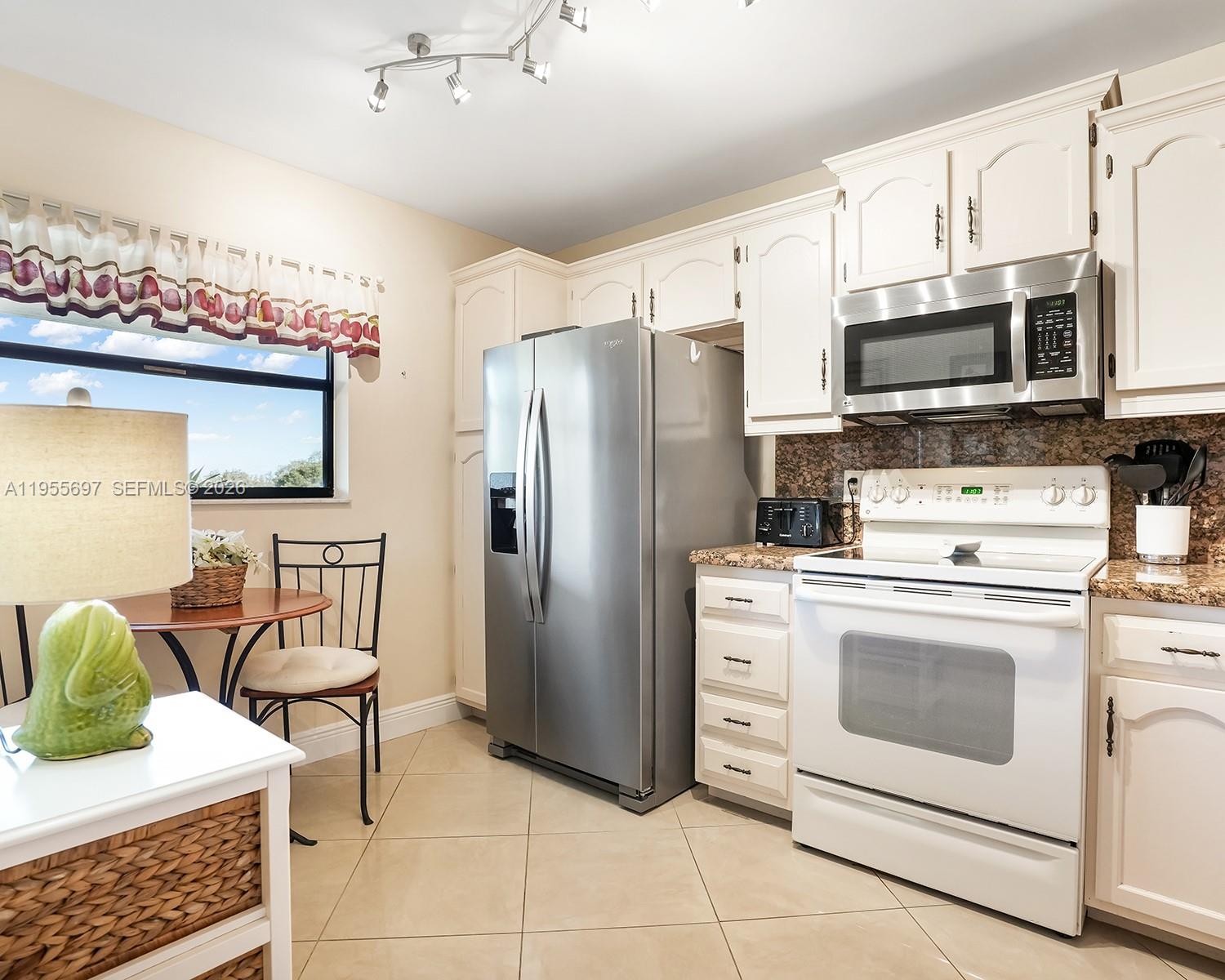 A kitchen features white cabinetry, stainless steel appliances, a white stove, and a small dining area — 3591 Environ Blvd # A404, Lauderhill FL 33319, LAUDERHILL, FL