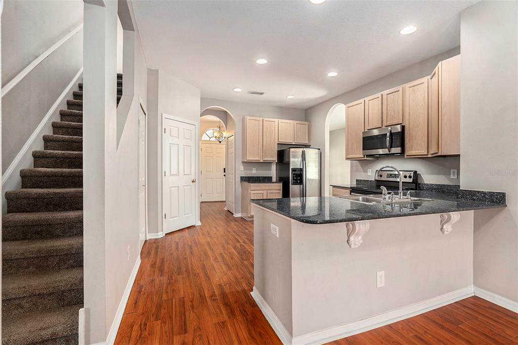 A kitchen with granite countertops and light wood cabinets overlooks a staircase and entryway — 3219 GIANNA WAY, LAND O LAKES, FL