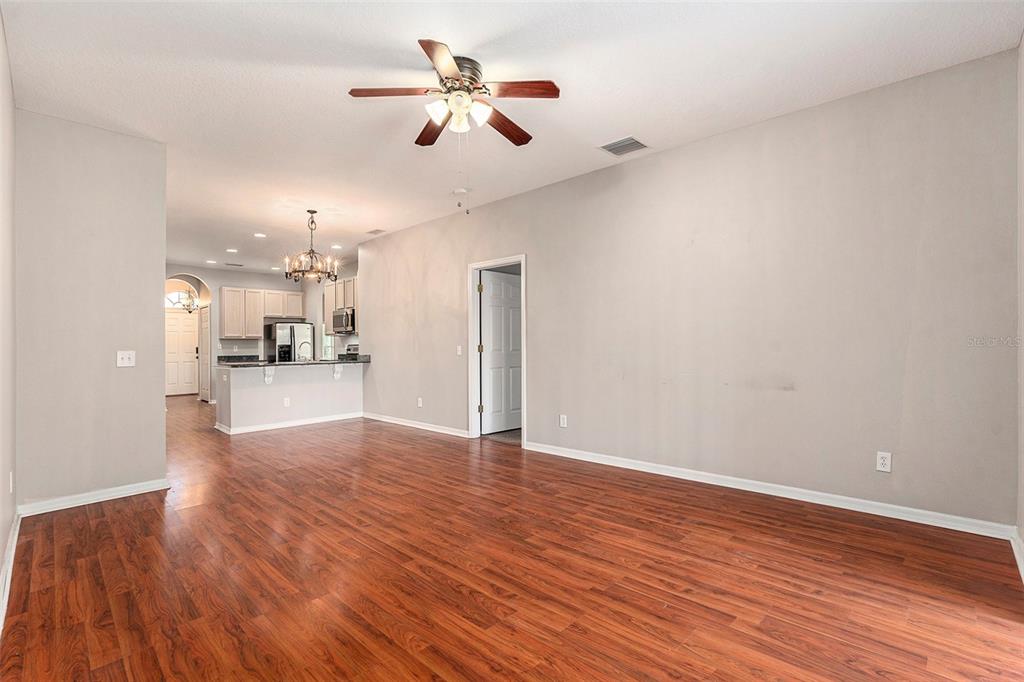 An open-concept living area features wood-look flooring, a ceiling fan, and an adjacent kitchen — 3219 GIANNA WAY, LAND O LAKES, FL
