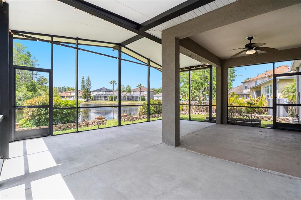 A screened-in concrete patio overlooks a lake with neighboring houses in the background — 3219 GIANNA WAY, LAND O LAKES, FL