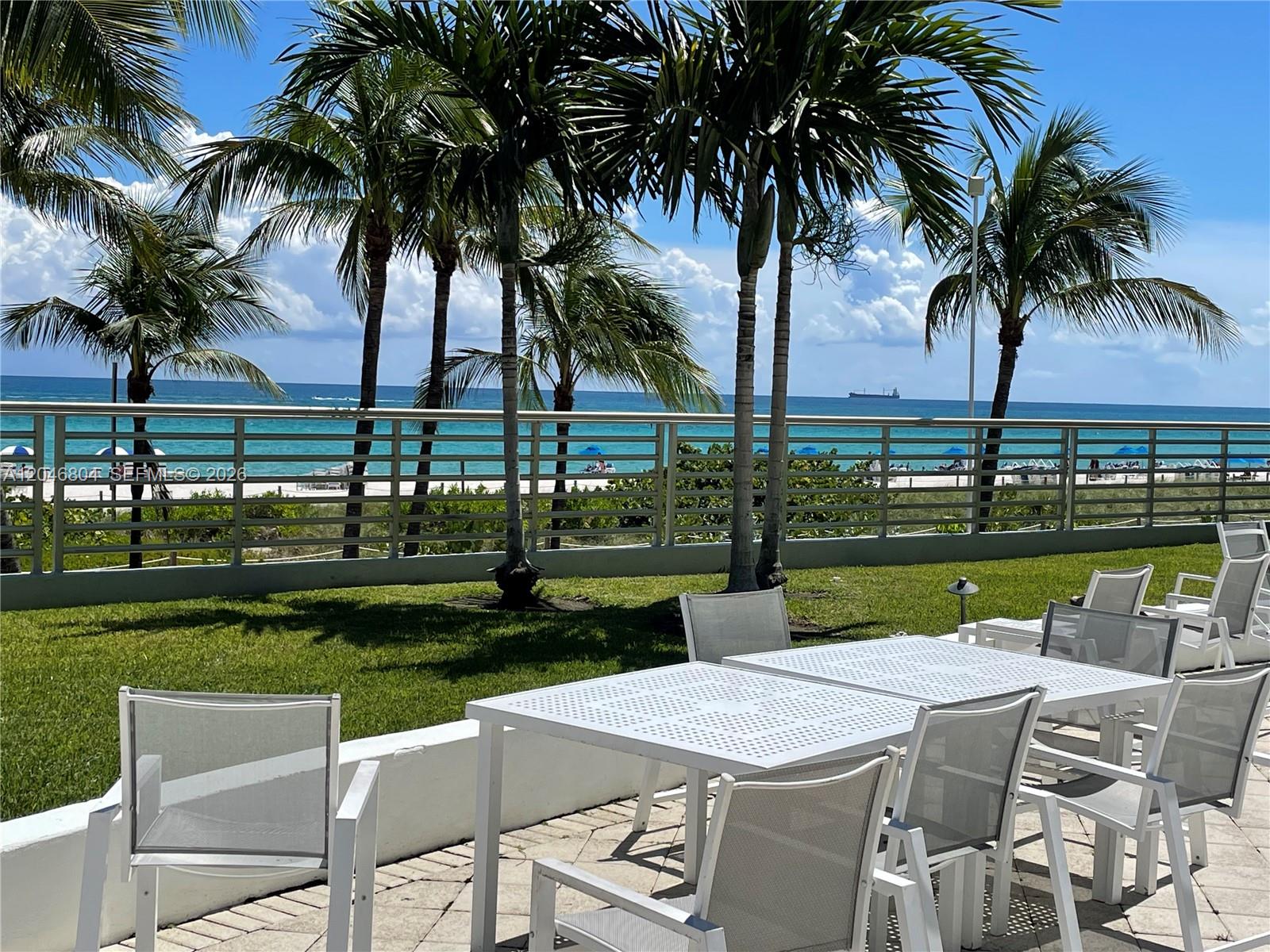 An outdoor patio features white metal tables and chairs overlooking a beach and ocean — 5151 Collins Ave # 1722, Miami Beach FL 33140, MIAMI BEACH, FL