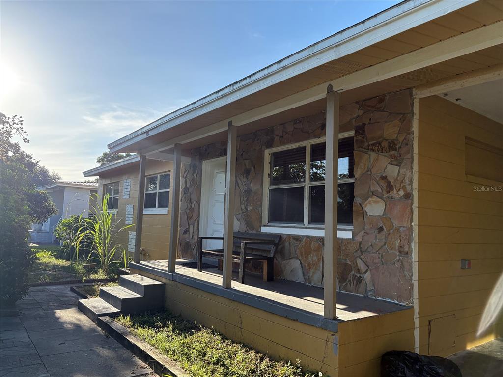 A yellow house exterior features a stone-faced front wall, a covered porch, and wooden posts — 3514 CALLOWAY DRIVE, ORLANDO, FL