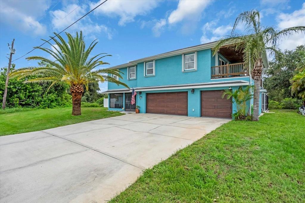 A two-story blue house features a two-car garage, a second-floor balcony, and palm trees — 27450 SAN MARCO DRIVE, PUNTA GORDA, FL