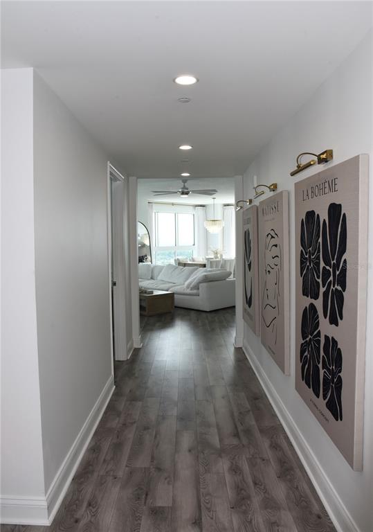 A hallway with wood-look flooring leads to a living room with a white sectional sofa — 241 RIVERSIDE DRIVE UNIT 2009, HOLLY HILL, FL