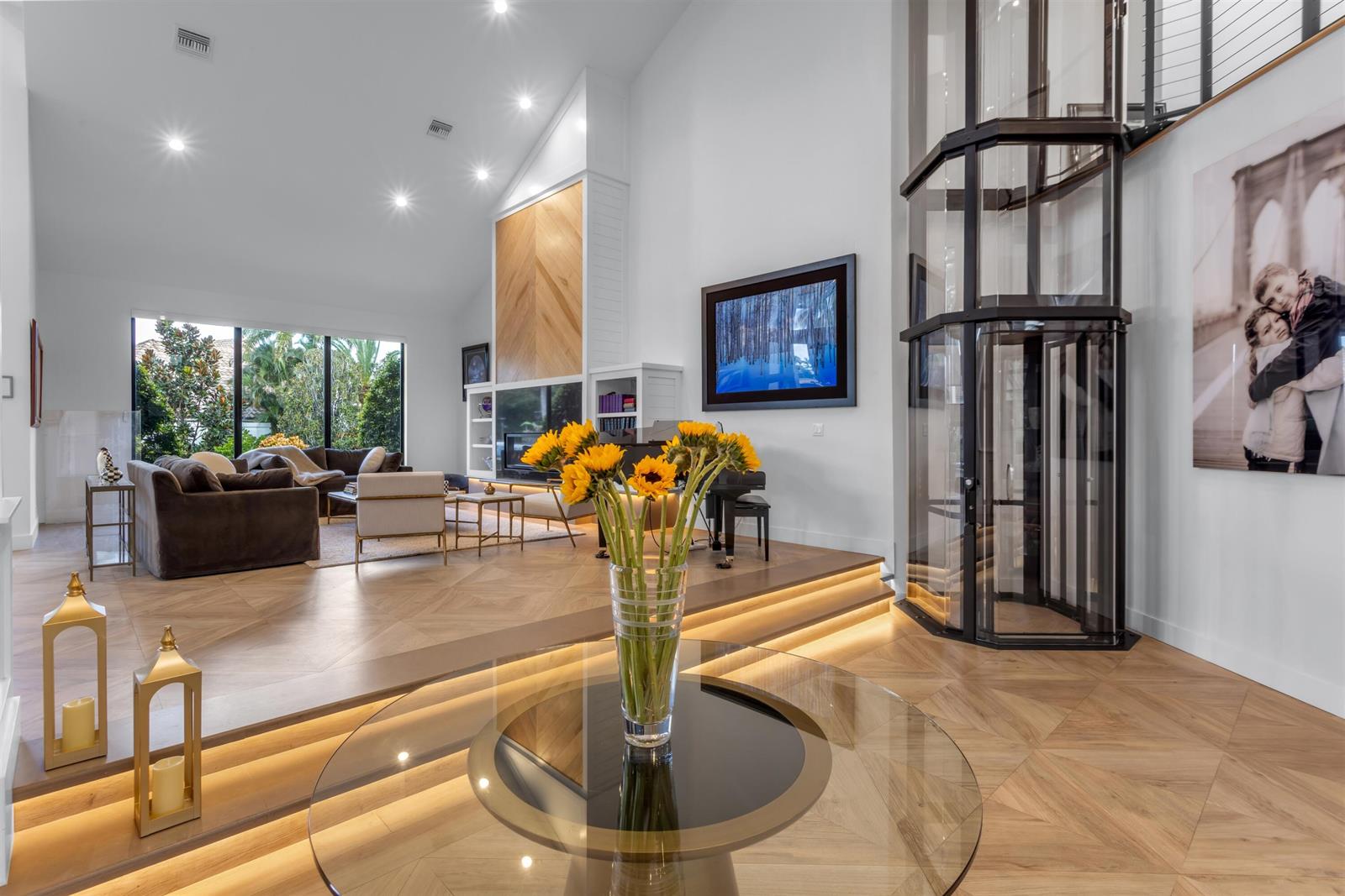 A living room with a glass elevator, hardwood floors, and a raised platform with sunflowers — 4698 Sanctuary Lane, Boca Raton FL 33431, BOCA RATON, FL