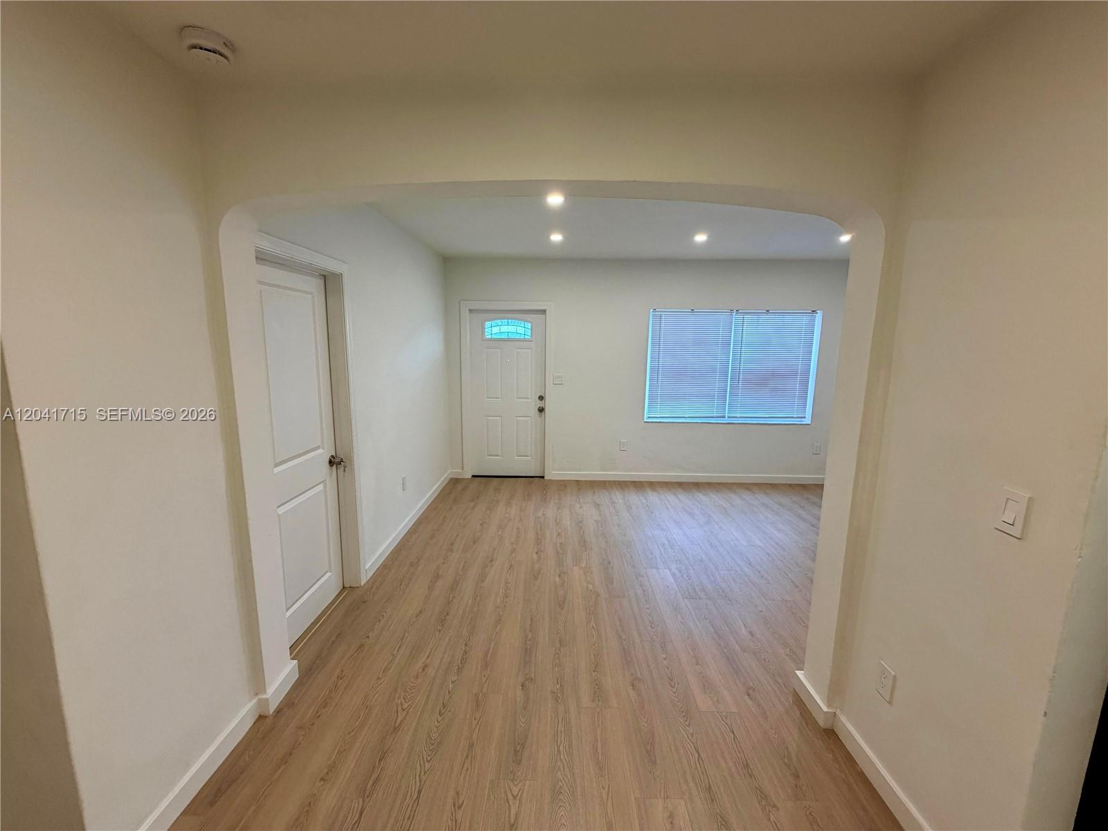An empty room with light wood-look flooring, white walls, a white door, and a window — 255 NW 32nd St, Miami FL 33127, MIAMI, FL