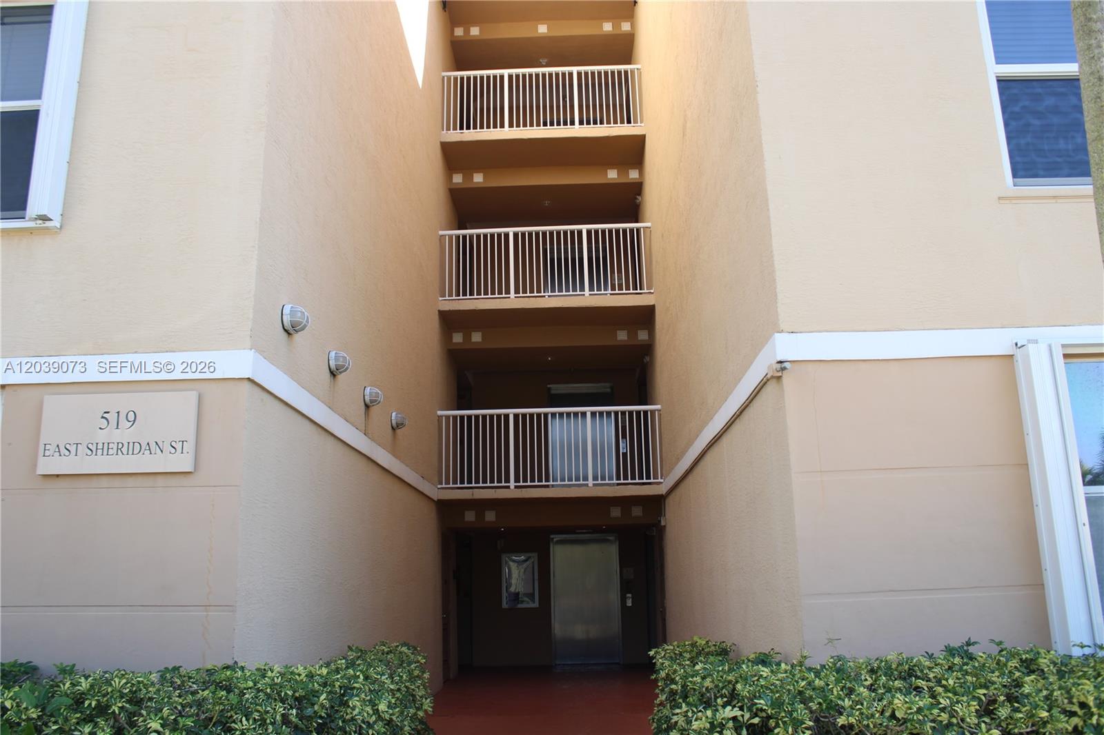 The exterior of a multi-story apartment building features stacked balconies and a ground-level elevator entrance — 519 E Sheridan St # 1082, Dania Beach FL 33004, DANIA BEACH, FL