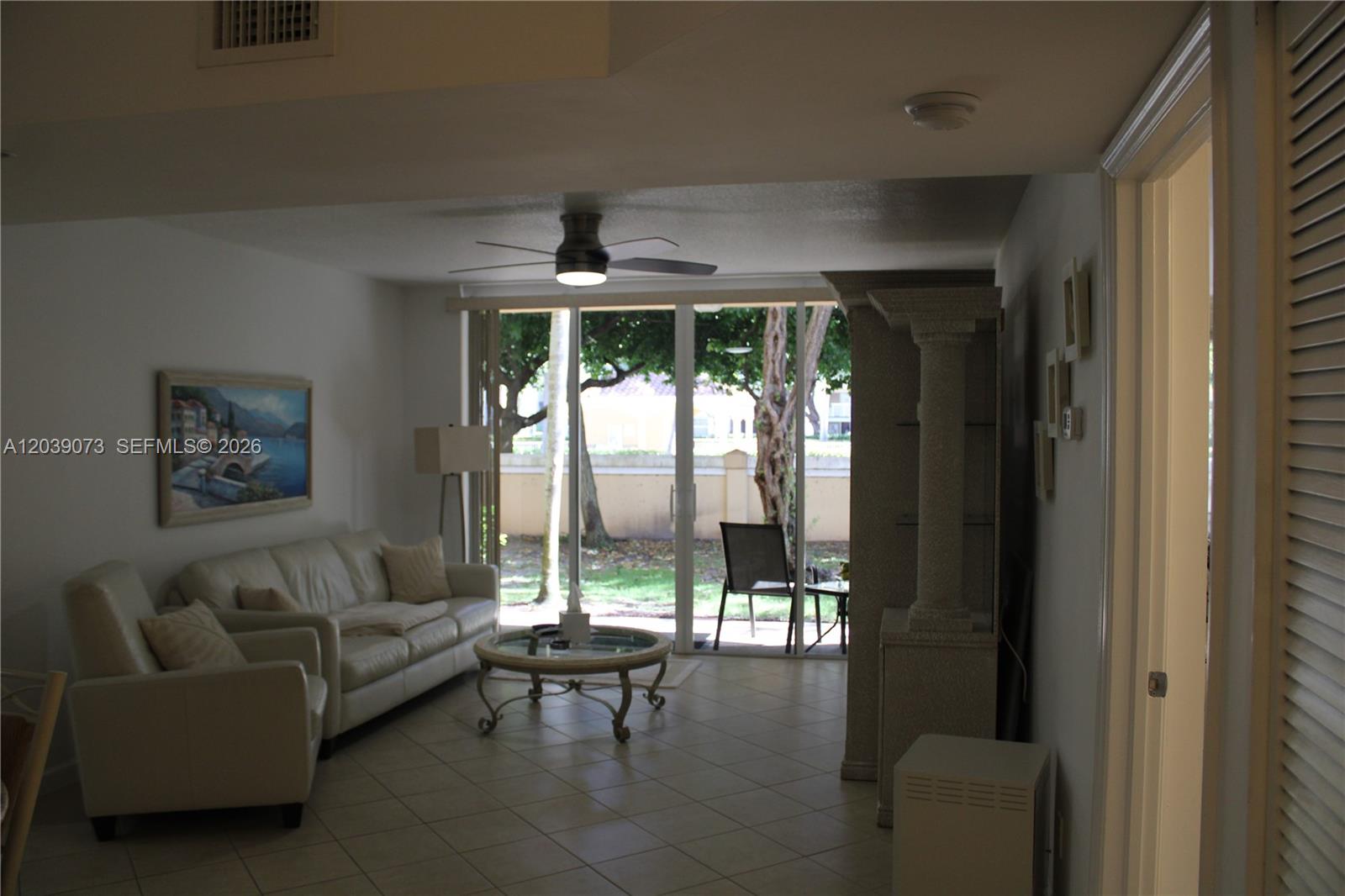 A living room features tile flooring, a white sofa, a ceiling fan, and sliding glass doors — 519 E Sheridan St # 1082, Dania Beach FL 33004, DANIA BEACH, FL
