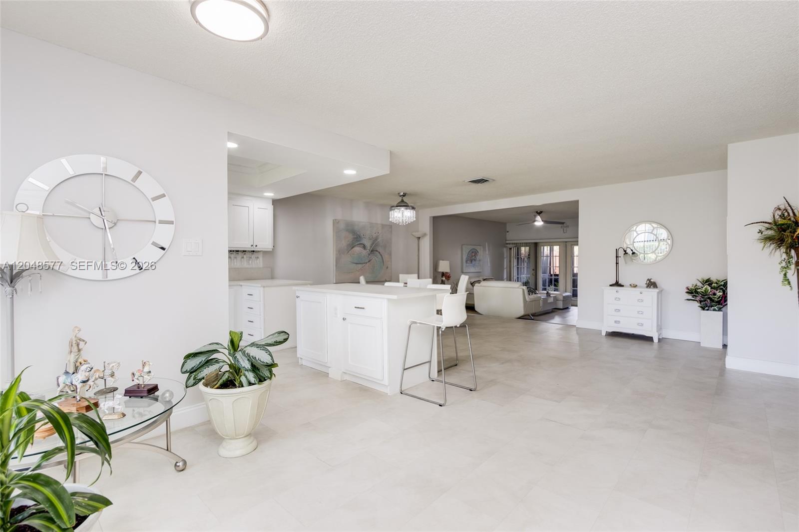 A bright, open-concept living area features a white kitchen island, tile flooring, and minimalist decor — 7032 SW 23rd St # 16, Davie FL 33317, DAVIE, FL