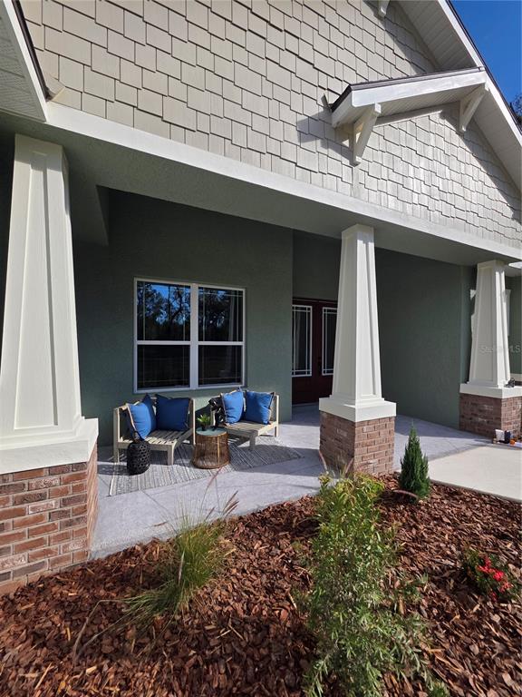 A covered front porch features two chairs, a small table, and white columns on brick bases — 13444 REPUBLICAN WAY, BROOKSVILLE, FL