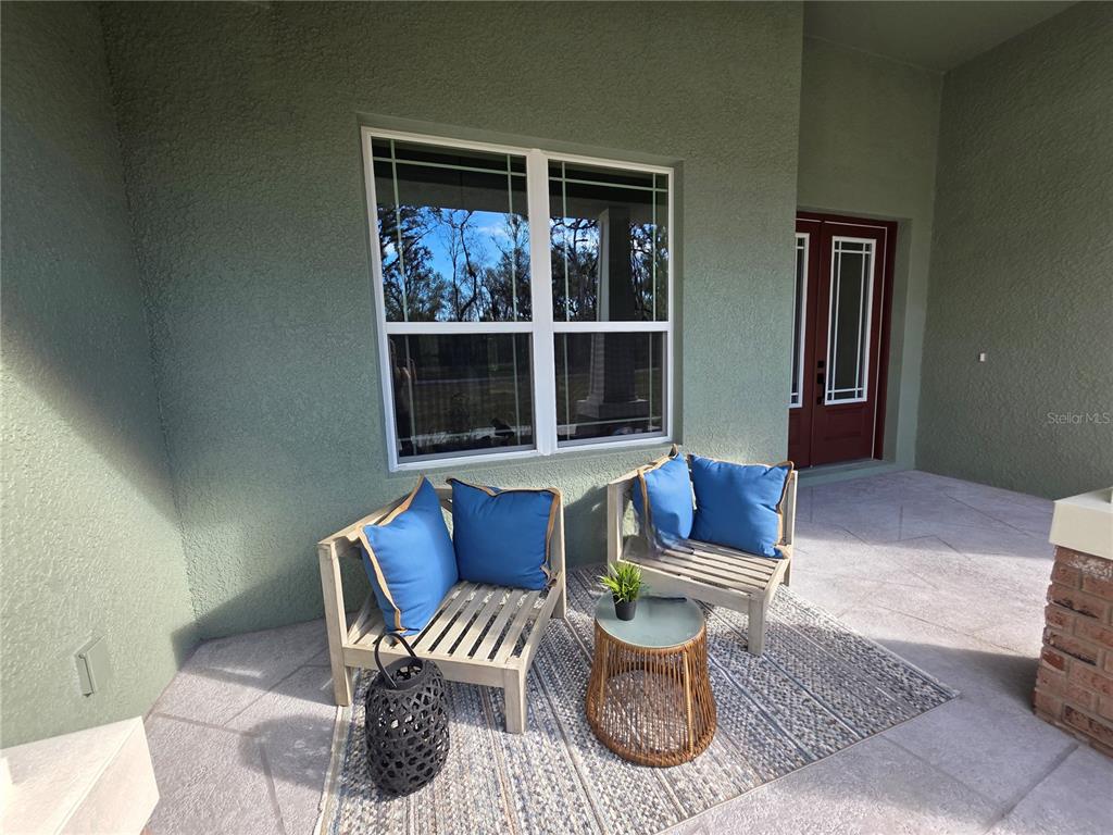 A covered patio features two wooden chairs with blue cushions, a small table, and a rug — 13444 REPUBLICAN WAY, BROOKSVILLE, FL