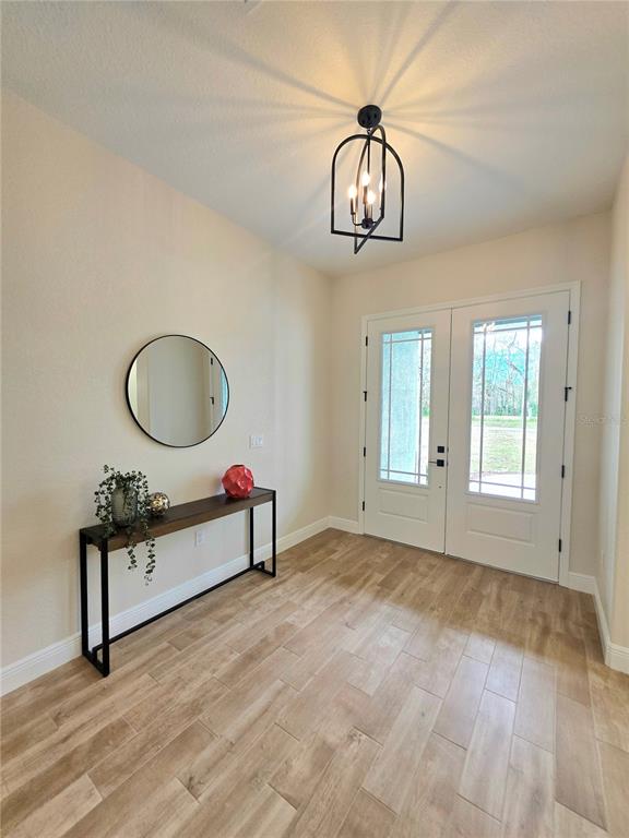 A bright entryway features a wood-look tile floor, a console table, a mirror, and a chandelier — 13444 REPUBLICAN WAY, BROOKSVILLE, FL