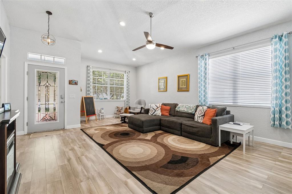 A living room features light wood-look flooring, a grey sectional sofa, and a patterned area rug — 11318 BRIDGE PINE DRIVE, RIVERVIEW, FL