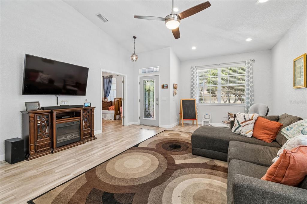 A living room features a vaulted ceiling, wood-look flooring, a sectional sofa, and a television — 11318 BRIDGE PINE DRIVE, RIVERVIEW, FL