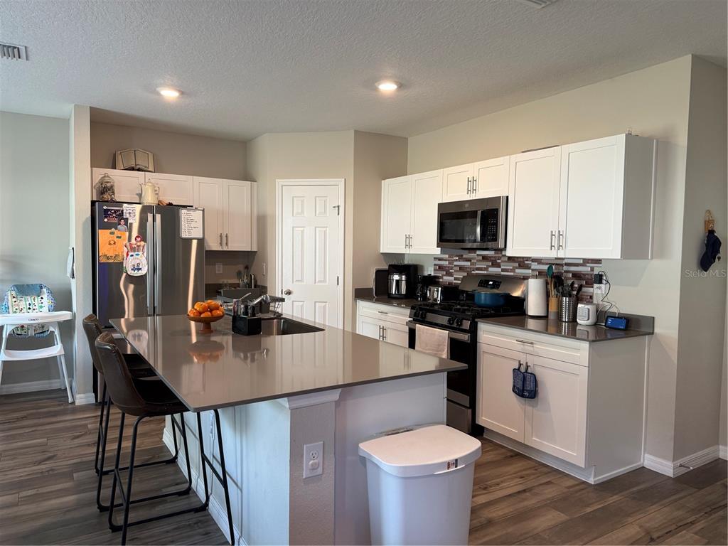A kitchen features white cabinets, a gray island with bar seating, and stainless steel appliances — 10960 3RD STREET, RIVERVIEW, FL