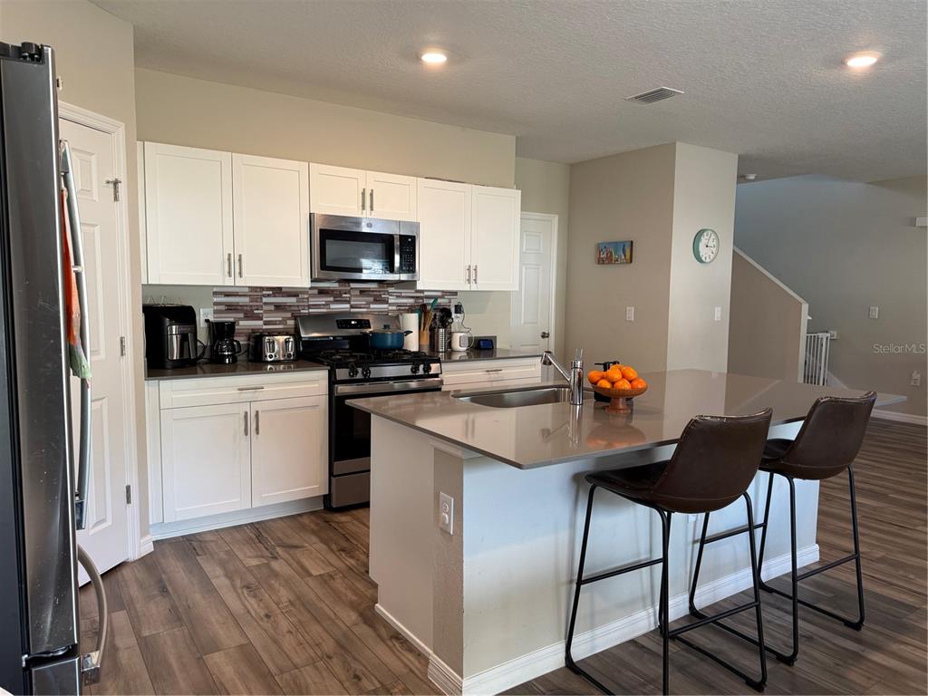 A kitchen features white cabinets, stainless steel appliances, a quartz island, and wood-look flooring — 10960 3RD STREET, RIVERVIEW, FL