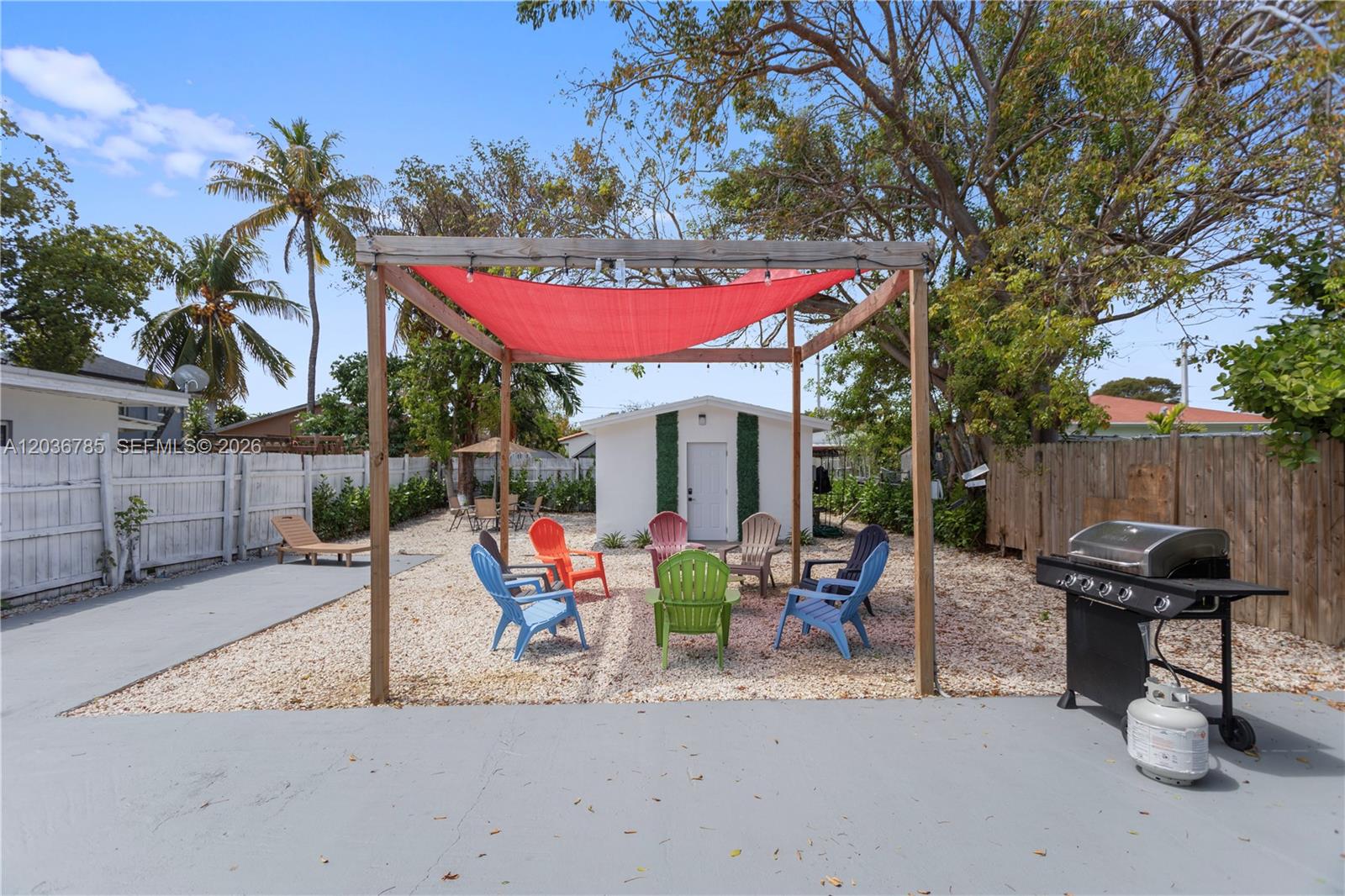 A backyard features a gravel patio with a red shade canopy, colorful chairs, and a grill — 3016 NW 22nd Ct # 3020, Miami FL 33142, MIAMI, FL
