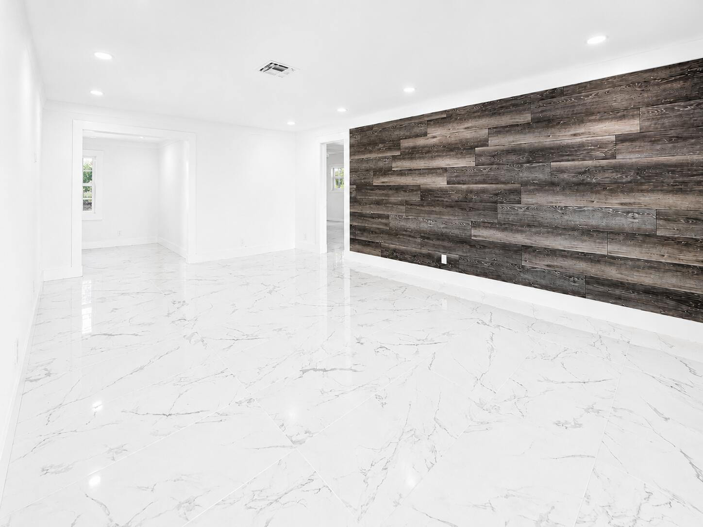 A bright room features white marble-look tile flooring and a dark wood-plank accent wall — 1009 Leisure Lane, Boynton Beach FL 33426, BOYNTON BEACH, FL