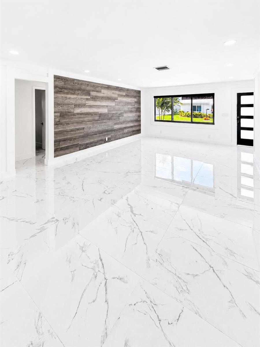 A bright, empty room features white marble-look tile flooring and a wood-paneled accent wall — 1009 Leisure Lane, Boynton Beach FL 33426, BOYNTON BEACH, FL