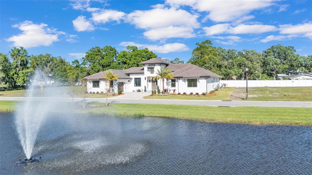 A white house with a brown roof sits behind a pond with a fountain — 5472 SHOREVIEW DRIVE, LAKELAND, FL