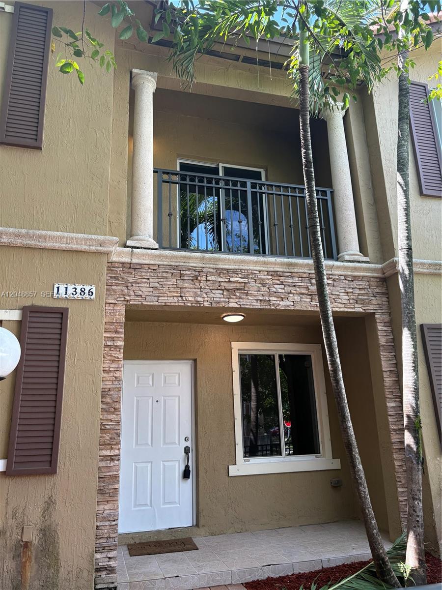The exterior of a two-story townhouse features a stone-accented facade, a balcony, and a front door — 11386 SW 230th Ter # 11386, Miami FL 33170, MIAMI, FL