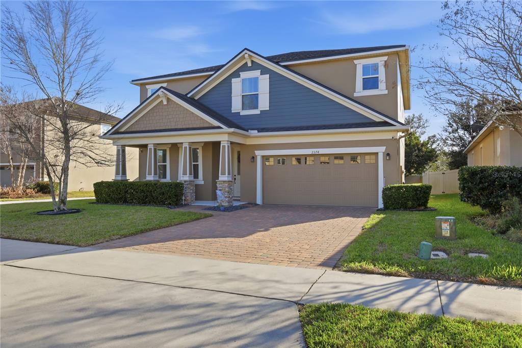 A two-story suburban house features a blue-accented gable, stone-based columns, and a paved driveway — 2374 KENNINGTON COVE, DELAND, FL