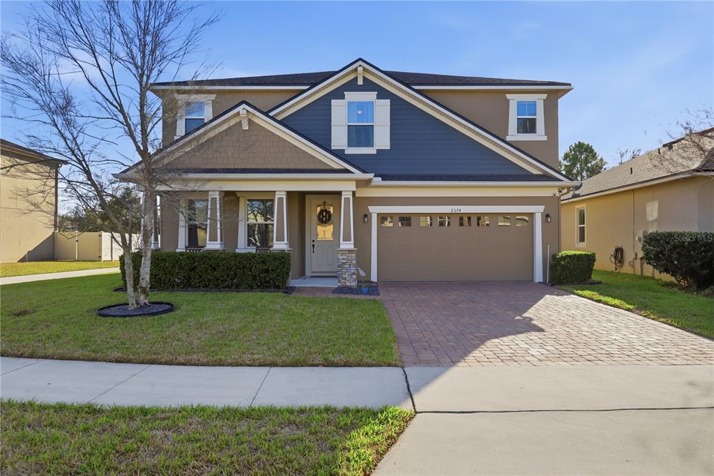 A two-story suburban house features a tan exterior, blue siding accents, and a paved driveway — 2374 KENNINGTON COVE, DELAND, FL