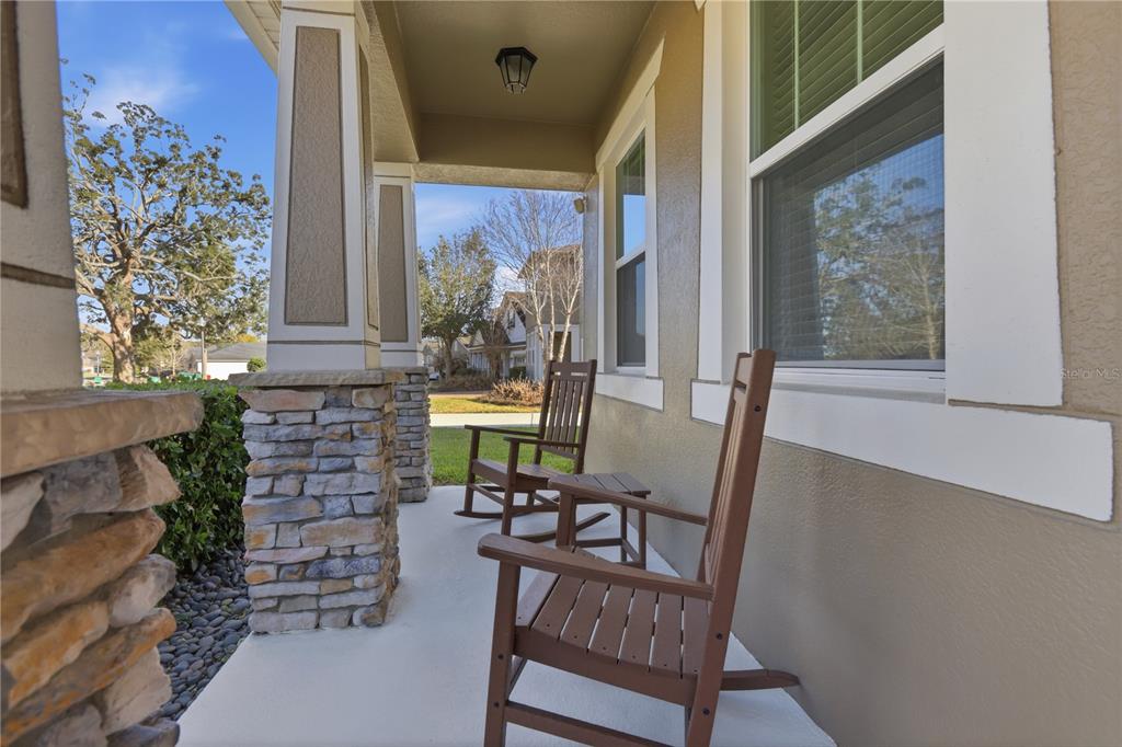 A covered front porch features two brown rocking chairs and stone-based support columns — 2374 KENNINGTON COVE, DELAND, FL