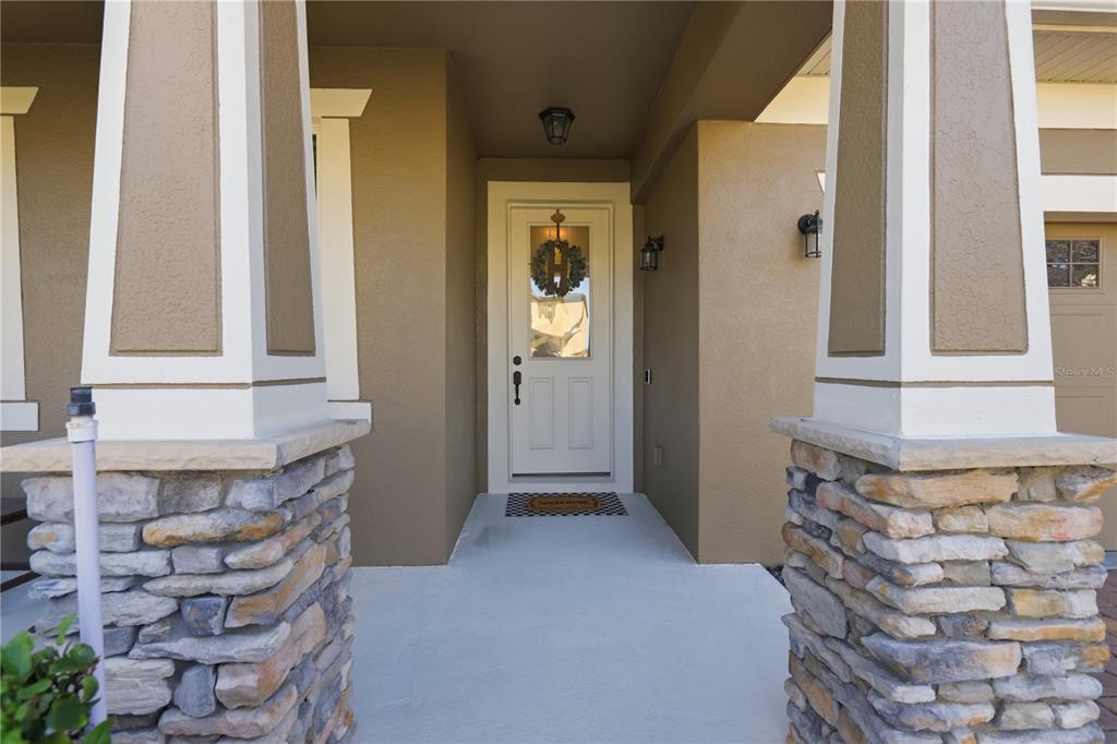 A covered front porch features stone-based columns and a white door with a glass insert — 2374 KENNINGTON COVE, DELAND, FL
