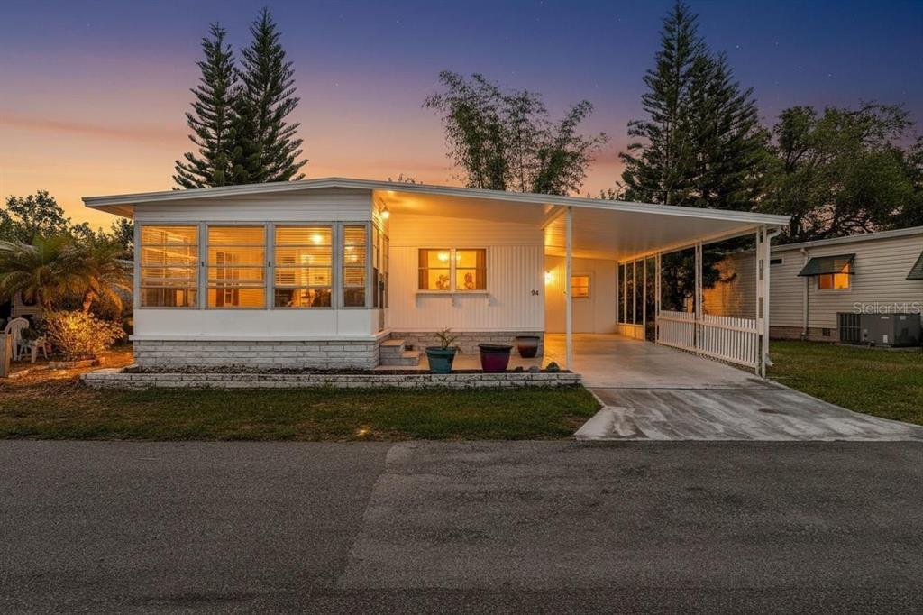 A white mobile home with a screened-in front porch and an attached carport at dusk — 94 SUGAR BEAR DRIVE UNIT 55, SAFETY HARBOR, FL