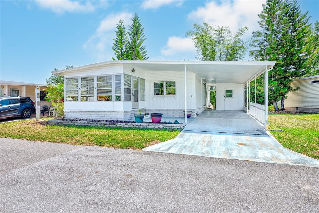 A white mobile home with a screened-in porch and a covered carport under a blue sky — 94 SUGAR BEAR DRIVE UNIT 55, SAFETY HARBOR, FL