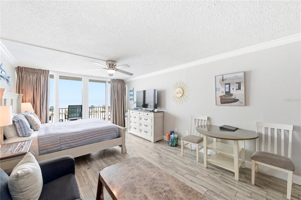 A bedroom with a bed, television, dining set, and a balcony overlooking the ocean — 9980 GULF BOULEVARD UNIT 211, ST PETERSBURG, FL