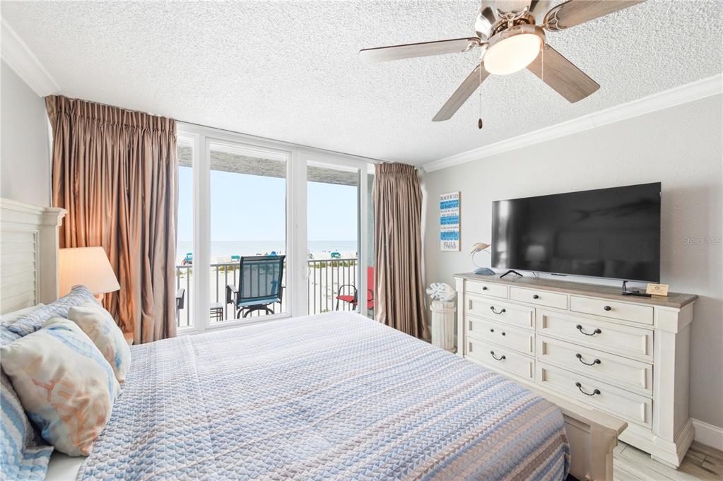 A bedroom features a bed, a dresser with a television, and a balcony overlooking the beach — 9980 GULF BOULEVARD UNIT 211, ST PETERSBURG, FL