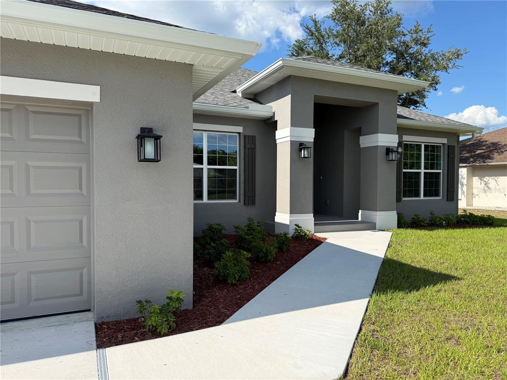 A gray stucco house exterior features a garage, a covered entryway, and a concrete walkway — 498 SANTIGUAY STREET, PUNTA GORDA, FL