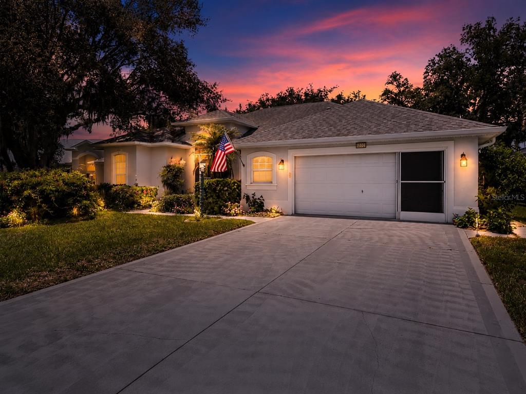 A single-story house with a two-car garage and an American flag at sunset — 5127 AURORA DRIVE, LEESBURG, FL