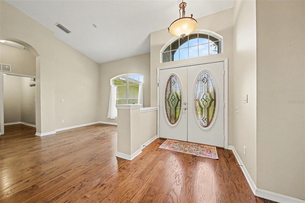 An entryway features hardwood floors, double front doors with glass inserts, and a vaulted ceiling — 5127 AURORA DRIVE, LEESBURG, FL
