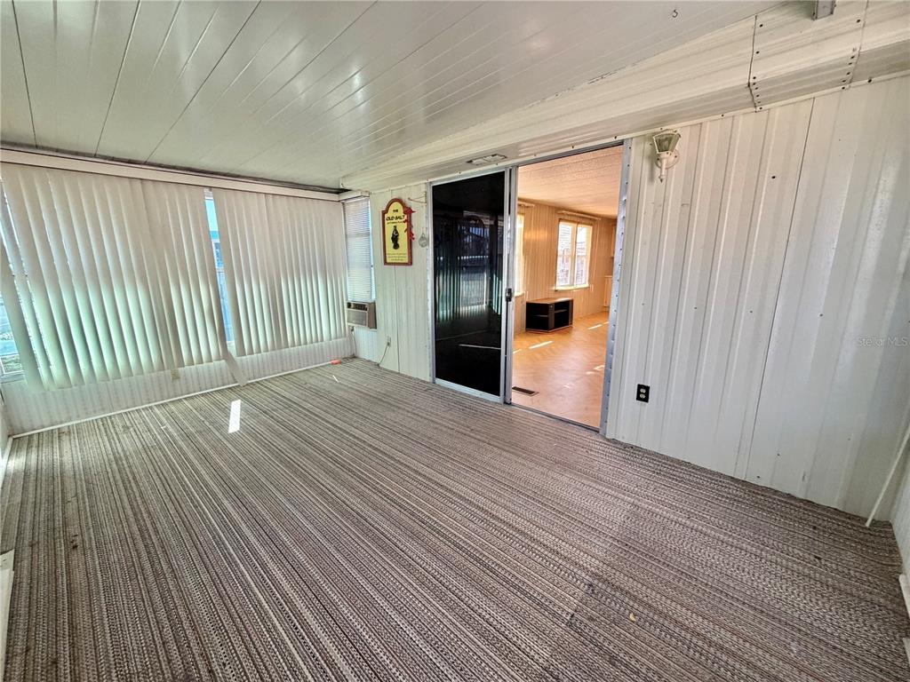 A sunroom with striped carpeting and vertical blinds leads into an interior living space — 353 PALO VERDE DRIVE, LEESBURG, FL