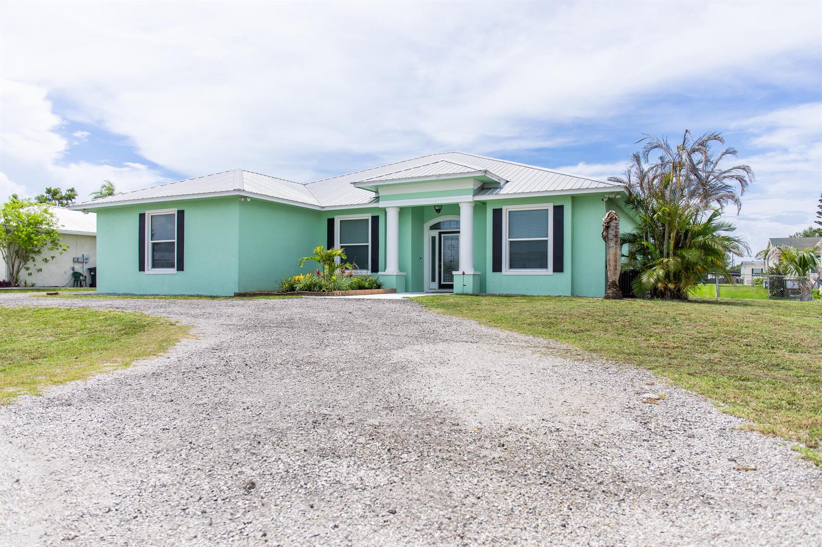 A light green, single-story house with a metal roof and a gravel driveway — 2406 SE 31st Street SE, Okeechobee FL 34974, OKEECHOBEE, FL