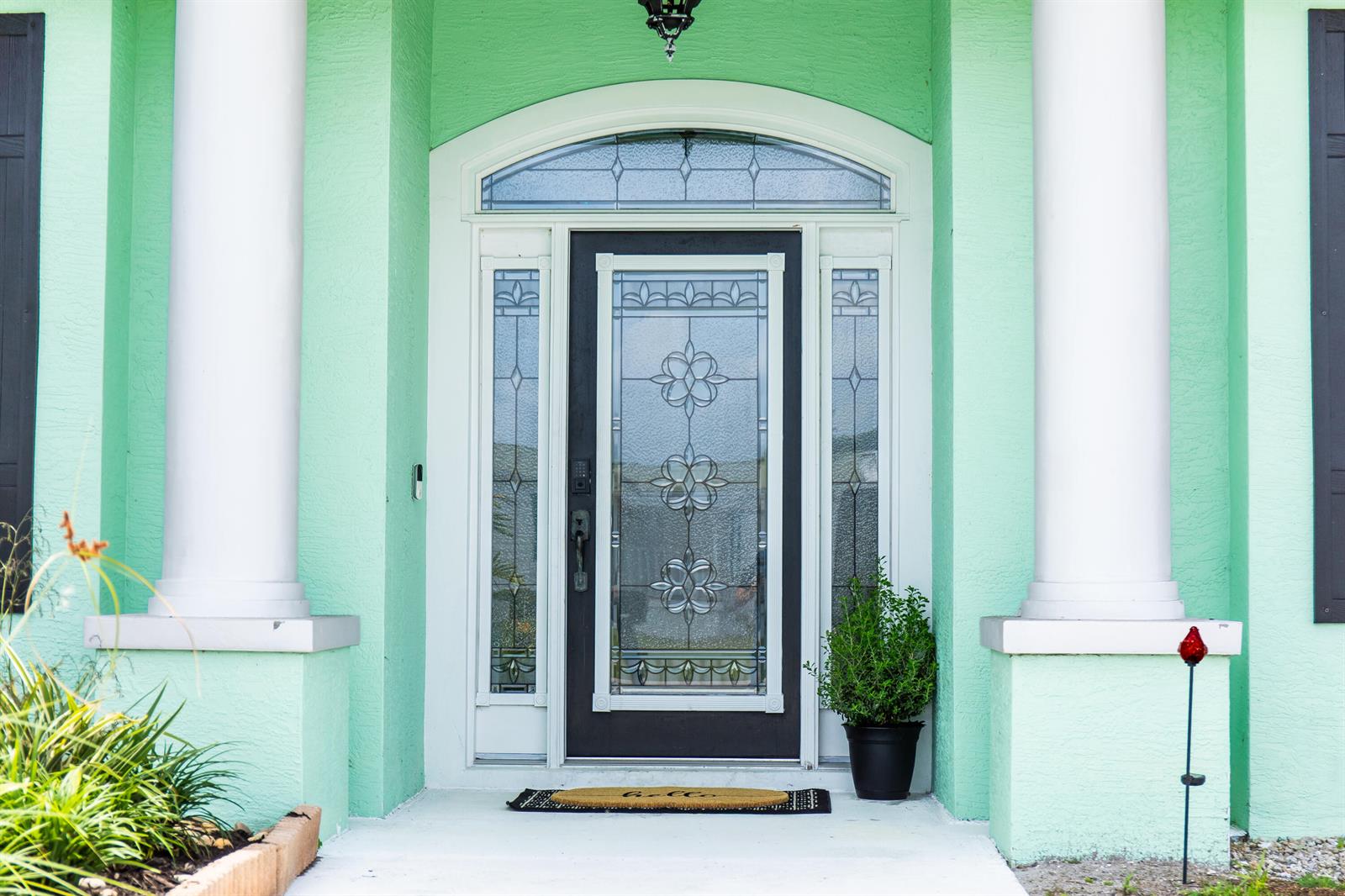 A front entrance with a dark door, glass inserts, and white columns on a mint-colored house — 2406 SE 31st Street SE, Okeechobee FL 34974, OKEECHOBEE, FL
