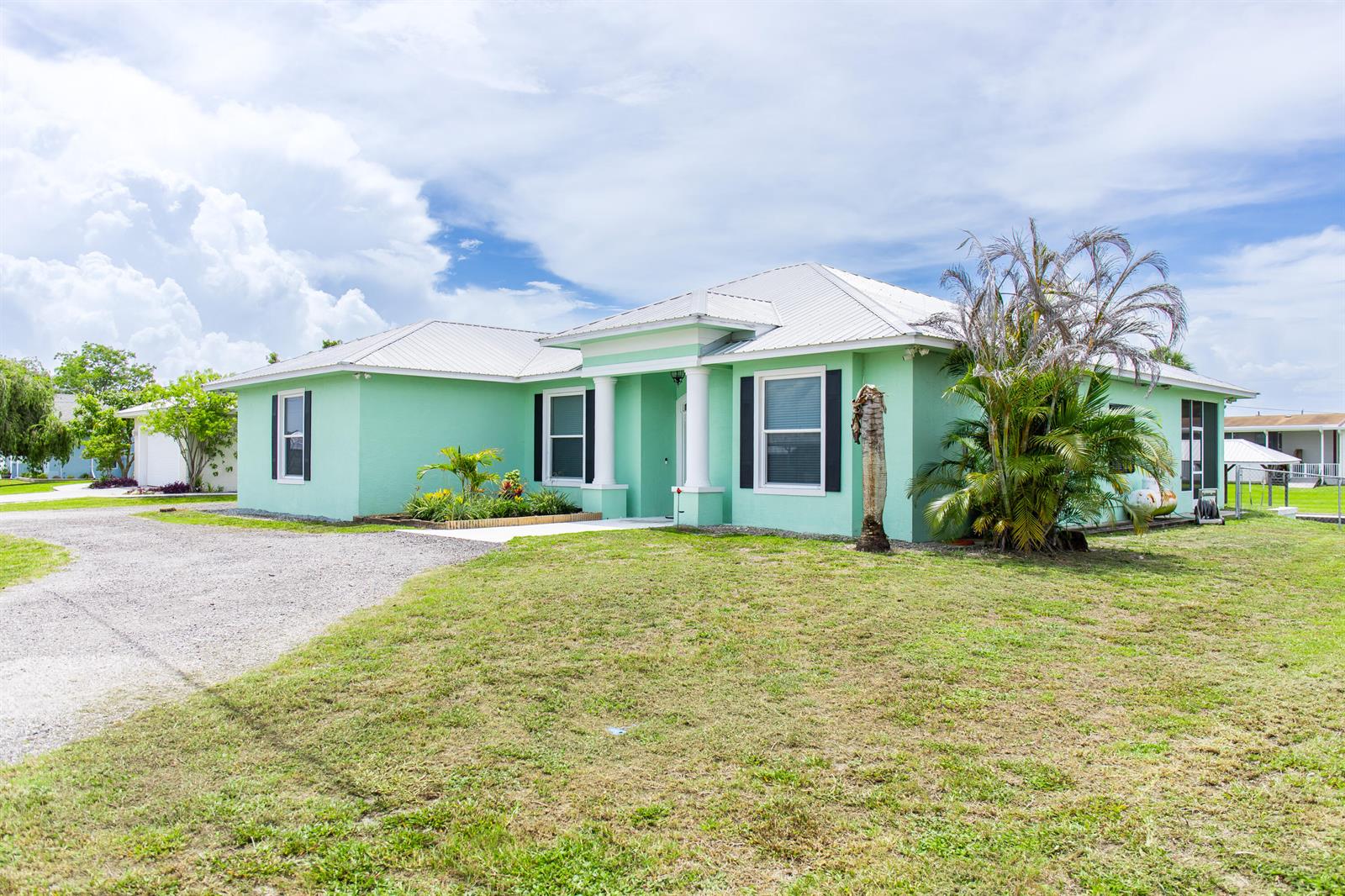 A light green, single-story house with a white metal roof and a gravel driveway — 2406 SE 31st Street SE, Okeechobee FL 34974, OKEECHOBEE, FL