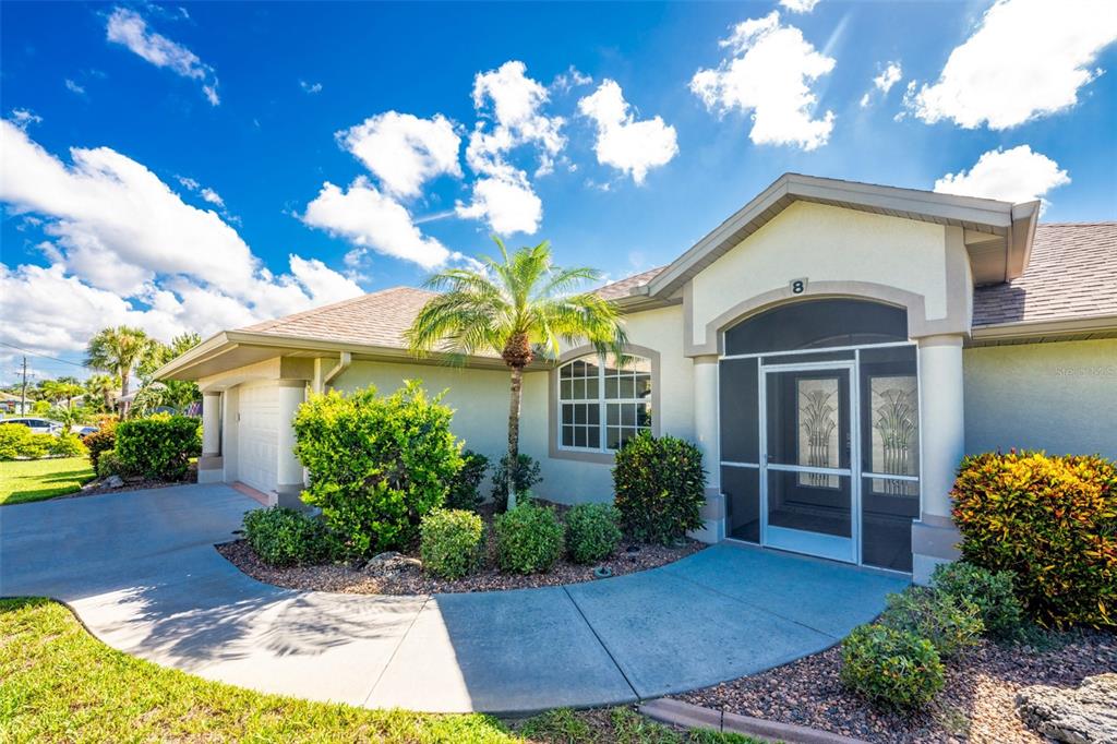 The exterior of a single-story house features a screened entryway, a palm tree, and landscaping — 8 SPORTSMAN ROAD, ROTONDA WEST, FL