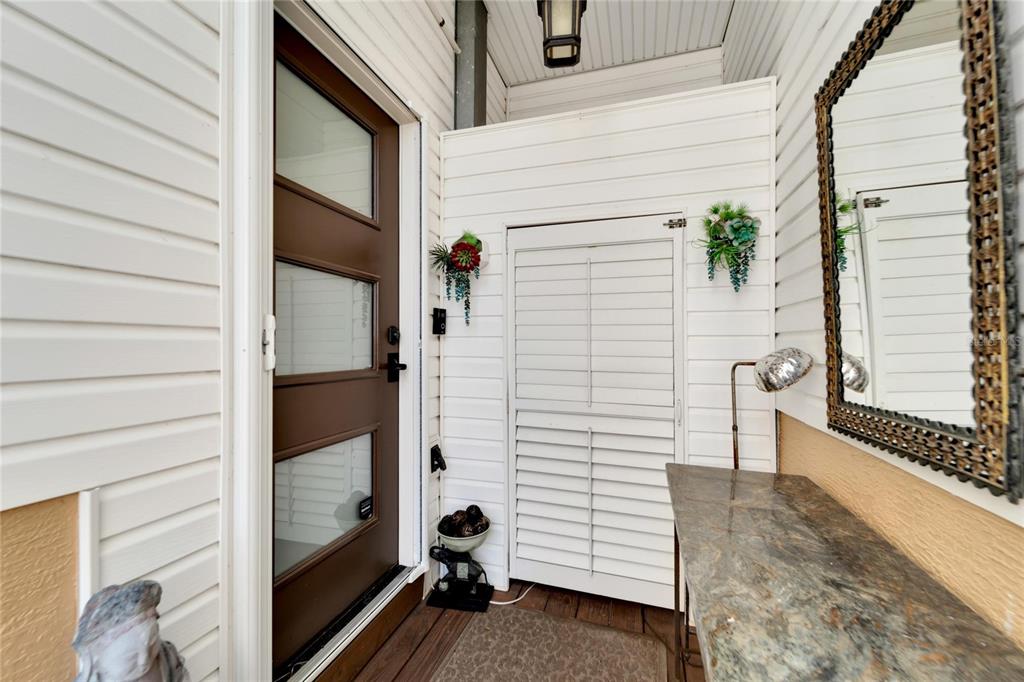 A covered entryway features a brown door, white siding, a console table, and a wall mirror — 5311 BOARDWALK STREET, HOLIDAY, FL