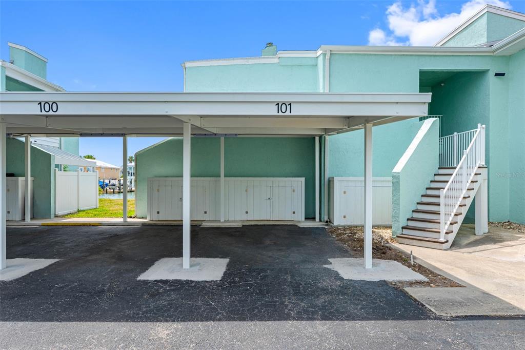 A covered parking area with storage units sits beside a building with an outdoor staircase — 1 WINDRUSH BOULEVARD UNIT 101, INDIAN ROCKS BEACH, FL